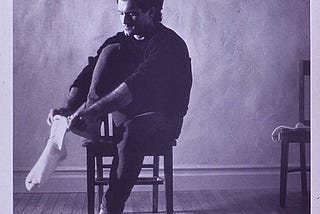 A man is sitting on a chair, putting on a sock. Text heading: “Putting on a condom is just as simple.”