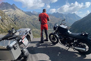 A motorcyclist standing in front of several motorcycles and looking out over distant mountain roads