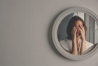 Woman in front of mirror with her hands over her eyes.