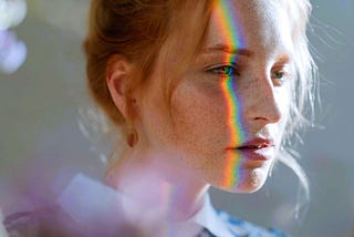 A young woman’s profile with a prism of rainbow light shining on her face.