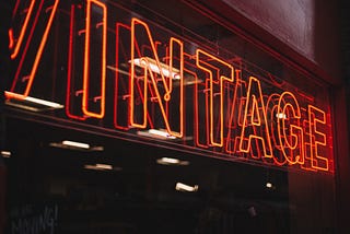 An orange neon sign on a black wall, reading “Vintage”