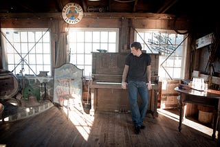 Gentry Bronson standing in front of the upright piano at Nick’s Cove in Tomales Bay, California