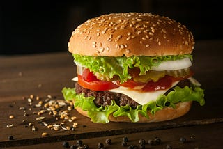 A large hamburger on a wooden table with pepper and sesame.