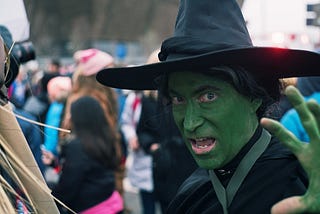 A woman dressed as a witch and wearing green face paint.