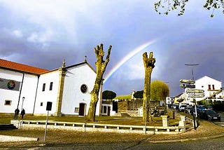 A white church with trees and a rainbow on the background.