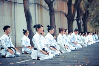 A row of people in karate uniforms sitting in meditation position