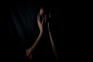 Woman’s face hidden by hands as she is scared, in the dark.