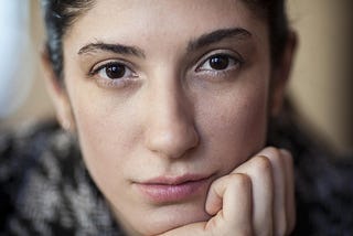 A young woman with brown eyes holding her chin in her hand.