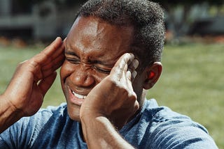 Man with his hands on either side of his head, as though his head is about to explode; he looks like he’s in a lot of pain