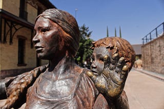 A bronze statue of a woman raising her hand in motion, with a child behind her left shoulder