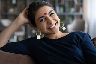 Happy, smiling young woman wearing a blue top sitting on couch, relaxed