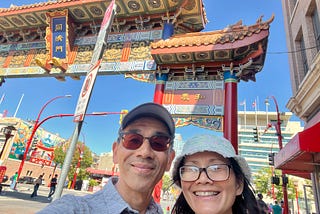 The author and his wife smiling and posing in front of the colorful gateway to the Victoria Chinatown.