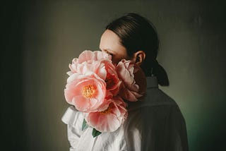 A woman with her face obscured by a bouquet of pink peonies.