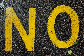 The word No painted in big, yellow letters on black asphalt