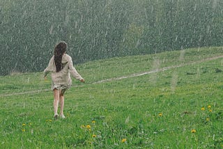 Woman enjoying the rain outside a grass field.