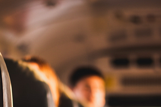 A child seated on the front of a bus looking back toward the rest of his classmates