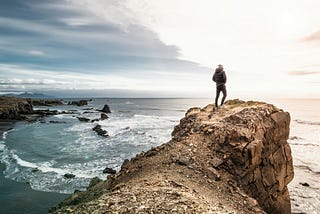 Man stands on a cliff overlooking ocean waters.