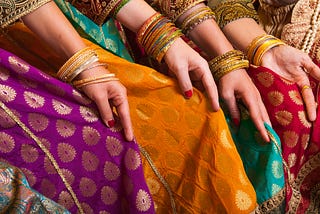 several women sitting in beautiful clothes from India, wearing gold bracelets