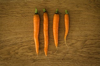 Top down view of four freshly washed carrots on a wooden counter top