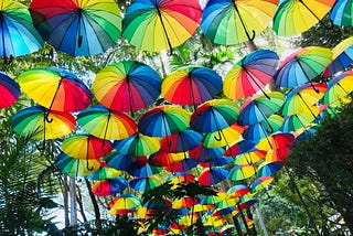 A canopy of rainbow-coloured umbrellas line a street.