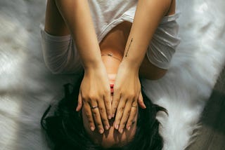 A woman holds her hands over her face against a white background. Photo by Anthony Tran on Unsplash