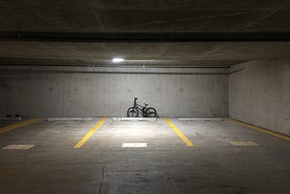 An empty parking garage, with an abandoned bicycle against one wall.