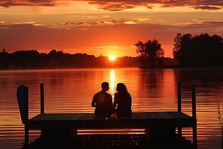 Two people sitting by a lake appreciating the sunset.