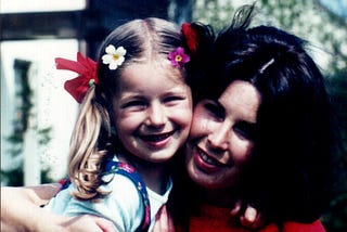 Mother hugging her young daughter who has red bows and flowers in her hair