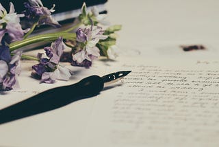 Image of a fountain pen and some purple flowers resting on paper