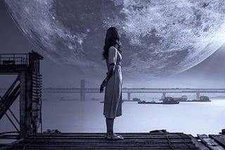 Woman standing by a shore in the dark, looking at the moon and clouds.