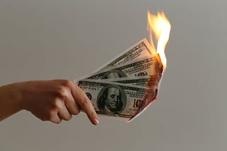 A hand holding four $100 bills that are on fire.