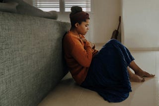 Anxious woman in orange sweater sitting on floor