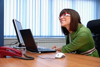 employee sitting at desk listening to bosses underhanded and unreasonable requests gritting her teeth with a smile