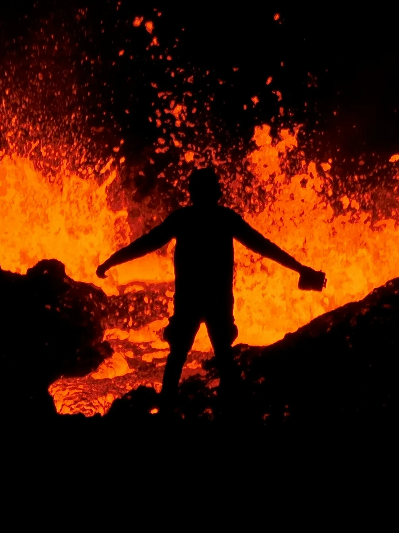 This image depicts a shadowy sillouhette holding a kerosene looking can. There is boiling lava all around them.