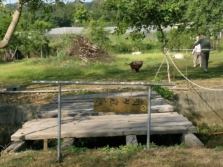 Two men walk around the yard outside of the Hong Kong Vipassana center, A sign reads in English and Chinese “student area ends here”