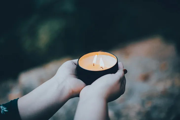 Cupped hands offer a candle with two flames