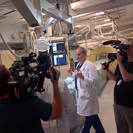 TV cameraman points video camera at Dr. Wood in a testing room in the Clinical Center