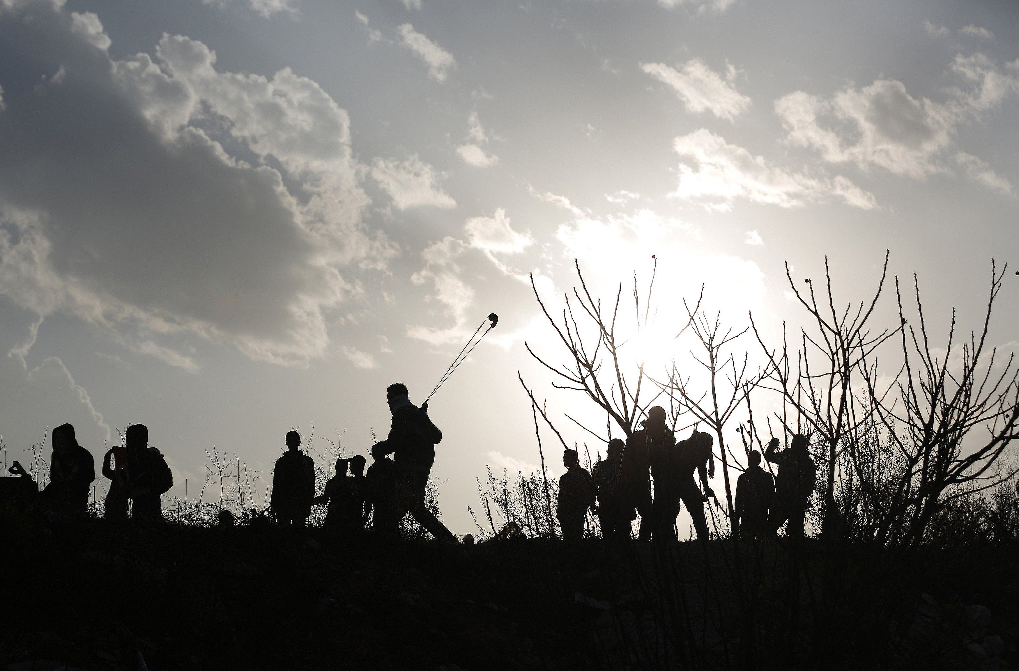 A Palestinian protester uses a slingshot to throw stones at Israeli troops as others gather during clashes near Israel’s Ofer Prison, near Ramallah