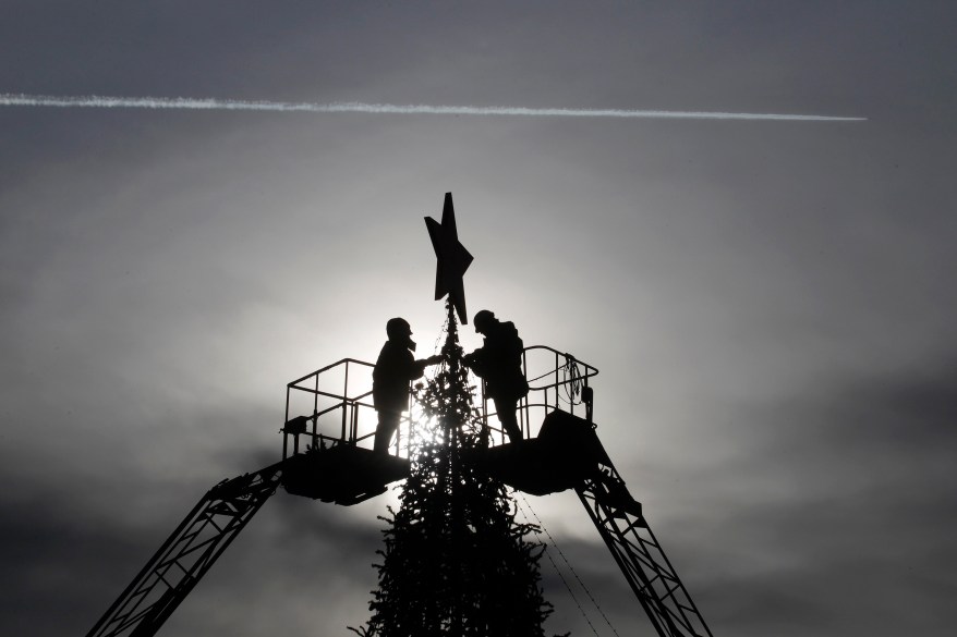 Workers decorate a Christmas tree at Lenin's Square as a plane passes by in Stavropol December 12, 2014. REUTERS/Eduard Korniyenko (RUSSIA - Tags: SOCIETY)