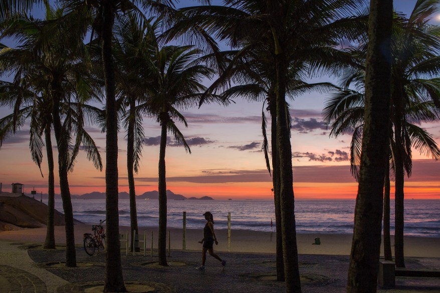 A woman walks between the palm trees before sunrise on Arpoador beach in Rio de Janeiro, Brazil, Thursday, Dec. 11, 2014. (AP Photo/Felipe Dana)