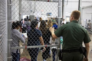 A Border Patrol agent watches people who've been taken into custody related to cases of illegal entry into the United States stand in line at a facility in Texas.