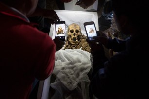 Relatives take cellphone pictures of skeletal remains of Fortunate Ventura Huamacusi in a coffin.