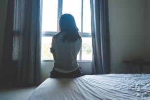 A woman sits on a bed looking out the window.