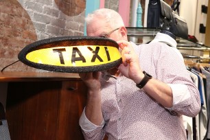 Ray Kelvin hides his face behind a Taxi sign at a Ted Baker event.