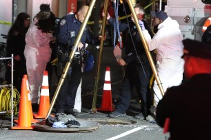 Cops work to retrieve the body of a man found dead in a manhole