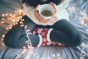 Woman sitting at home legs crossed on bed, holding a cup of coffee with christmas decorations.