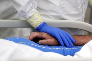 A member of the medical staff holds the hand of a patient suffering from the coronavirus disease