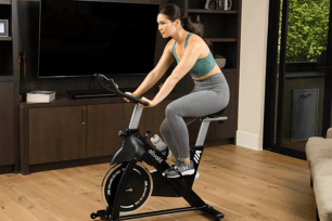 A woman in leggings and a sports bra on a cycle bike in her home