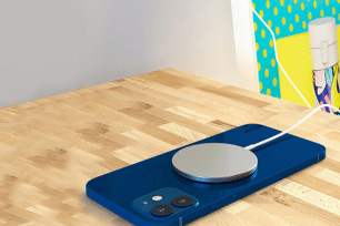 A blue iPhone face down on a desk with a silver wireless charger pad on it