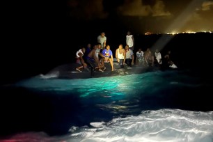 Survivors of a migrant boat that capsized perch on the overturned vessel off the coast of New Providence island, Bahamas July 24, 2022.